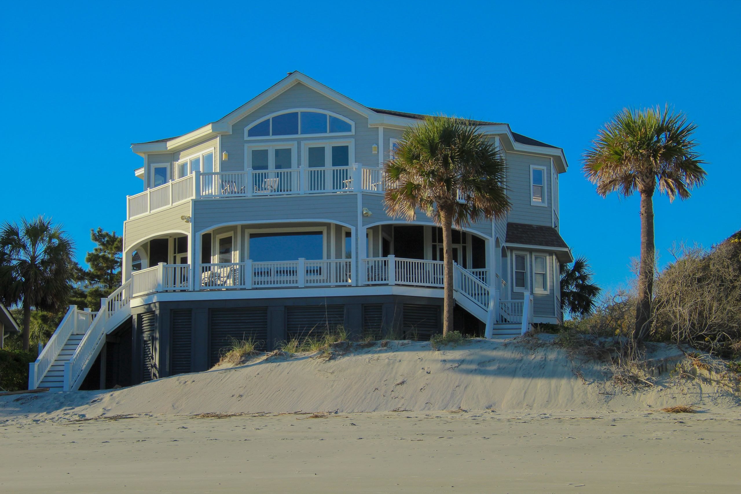 An elevated coastal home with wraparound porches and palms, in bright daylight
