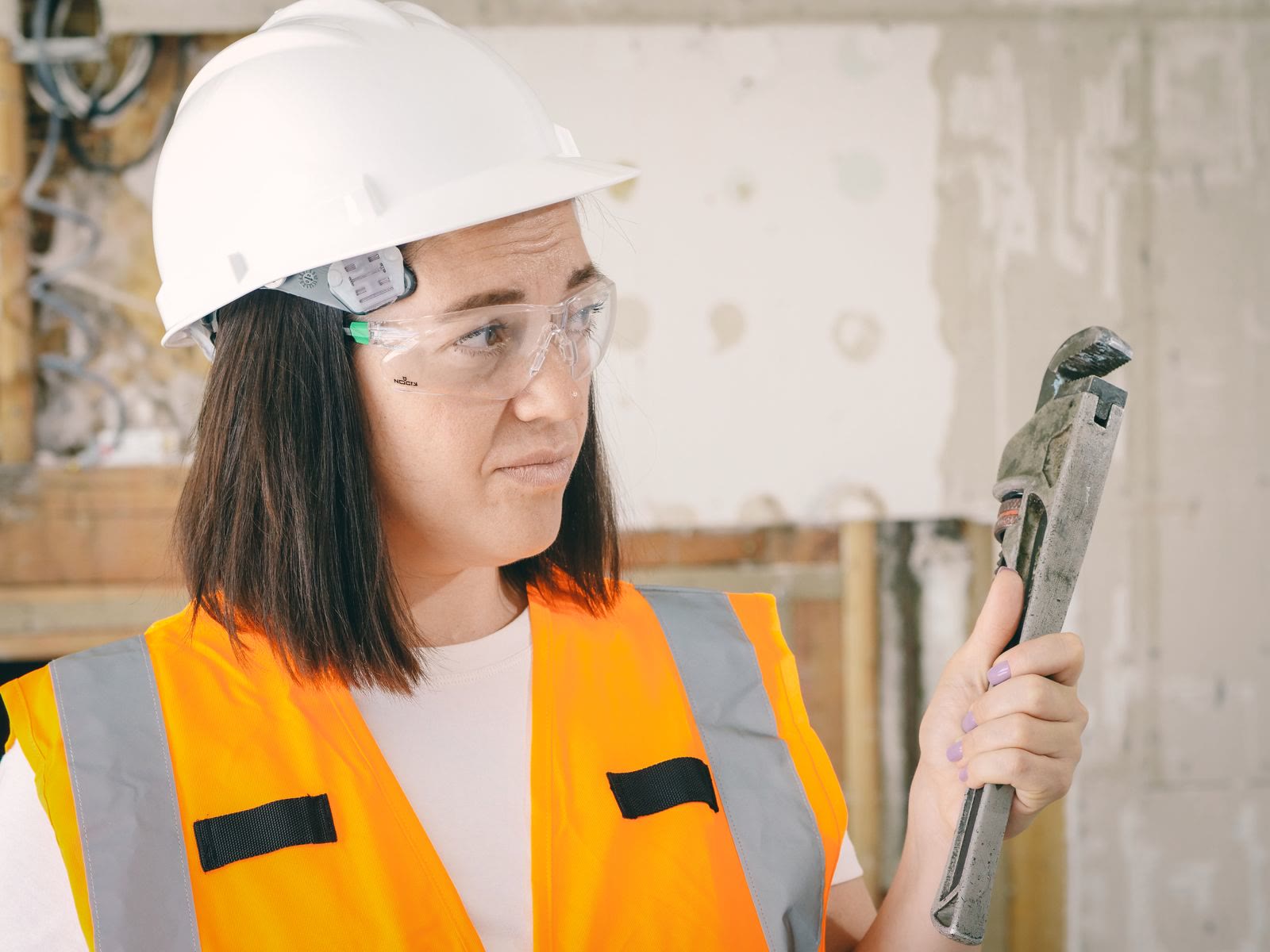 A plumber in work gear holding a pipe wrench inside a home